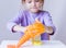 A girl in a lavender long sleeve stretches an orange slime with her hands