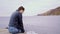 A girl in a leather jacket sits on the edge of a wooden bridge dangling legs. The girl is sitting on the pier. River