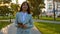 Girl in light suit goes to work with tablet in hand. Beautiful female businesswoman walks along alley in park and checks