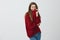 Girl like comfortable and loose clothes. Studio shot of good-looking charming woman in red sweater pulling collar while