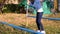 Girl like equilibrist walking on narrow crossbar with long pole in autumn park