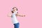 Girl listening to music in headphones on pink background. Cute child enjoying happy dance music, close eye`s and smile