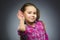 Girl listens. child hearing something, hand to ear gesture on grey background.