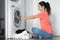 A girl loads dirty laundry into a washing machine while sitting on the floor in an apartment. Laundry day, housework