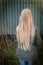 Girl with long blonde hair from behind by a rusty green wall