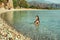 A girl with long dark hair swims in the sea on a beautiful deserted beach with green mountains along the banks.