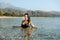 A girl with long dark hair swims in the sea on a beautiful deserted beach with green mountains along the banks.