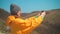 A girl with long dark hair in a yellow jacket, a gray cap, glasses is standing on mountain and making a photo on phone.