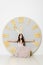 A girl with long hair in a beige dress sits near a large clock with a golden dial. Conceptual image. Time. White background and