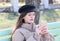 A girl with long hair in a jacket pokes a finger at the smartphone screen while sitting on a bench in the park