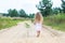 A girl with long hair walks along a rural road, portrait from back. A walk in a fresh air in solitude.