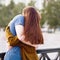 Girl with long thick dark hear embracing redhead boy on bridge, teen love at sunset