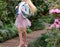 Girl with long white hair in a denim jacket walks in a flowering garden