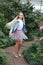 Girl with long white hair in a denim jacket walks in the garden with blooming azalea