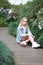 Girl with long white hair in a denim jacket walks in the garden with blooming azalea