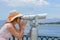 Girl looking thru public binoculars at the seaside wearing pink