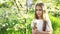 A girl looks at the camera with concentration and holds a white dandelion on a background of green grass in garden