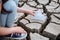 The girl lowers the paper boat onto the dry, cracked ground.