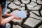 The girl lowers the paper boat onto the dry, cracked ground.