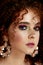 A girl with lush curly red hair. Close face with bright make-up and massive earrings. Purple shadows.