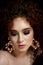 A girl with lush curly red hair. Close face with bright make-up and massive earrings. Purple shadows.