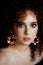 A girl with lush curly red hair. Close face with bright make-up and massive earrings.Purple shadows. Bare shoulders.