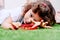A girl lying on the grass with her face pressed to the ground is scrutinizing a toy with her eyes