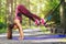 Girl in magenta sportswear exercising in the park while balancing on a yoga mat with her fits in the elastic straps