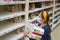 Girl makes stock of products. Reaching food shelf