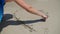 The girl is making a drawing on the sand. The sea wave is washing away the pattern on the sand on a sunny day