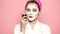 Girl with a mask on her face eating cucumber on pink background. Woman wearing face mask. Face care, facial beauty