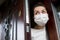 A girl in a medical mask cautiously peeks out of a house during a virus pandemic