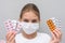 A girl with a medical mask on her face holds blisters with medicines