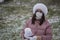 A girl in a medical mask and winter clothes on a walk in the park. Holds a ball of snow in his hand. The ground is covered with th