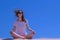 Girl meditate looks around sits sandy beach on blue sky background yoga pose.