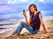 Girl with mobile phone sitting on sand near sea.