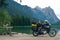 Girl motobiker in protective turtle jacket stands on the beach with tourer motorcycle. Extreme travel vacation, motorcyclist