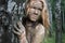 A girl with a mud mask peeps out from behind a birch trunk at an ecological resort