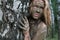 A girl with a mud mask peeps out from behind a birch trunk at an ecological resort