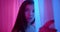 Girl in neon looks at the camera around the corner light night portrait flirts curtains pink blue