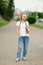 Girl with notebook in hand stands on sidewalk, long white hair, white skin, friendly look