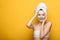 Girl with nourishing facial mask touching towel on head on yellow background