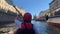 A girl with an oar floats on a red kayak, view from the back.