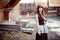 Girl in old fashioned outfit wearing flat cap at courtyard of wooden barracks, retro look.