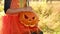 A girl in an orange dress holds a  empty sinister pumpkin in her hands on Halloween day.