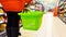 Girl in orange jacket with empty green shopping basket walking between the shelf in a store