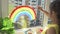 Girl painting rainbow on window during quarantine