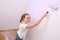 Girl paints wall in lilac color with roller