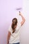 Girl paints wall in lilac color with roller