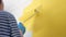 Girl paints wall with roller in her right hand in yellow. She is wearing striped shirt and blue gloves. Close-up view